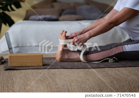 Senior woman practicing yoga, doing seated forward bend pose, paschimothanasana using belt. 71470548