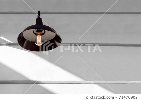 iron black loft style light with an edison lamp with threads shining warm light on a white wall with sunlight and copy space, decorative object lantern, nobody. 71470902