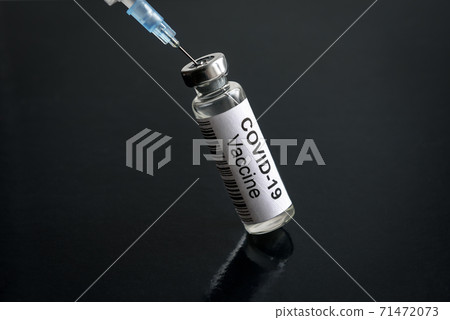 COVID-19 coronavirus vaccine in bottle and syringe on black desk 71472073