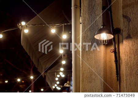 retro loft style street lantern on a building facade illuminates a city street at night, a closeup of a designer edison lamp with valve and garland light bulbs. 71473049