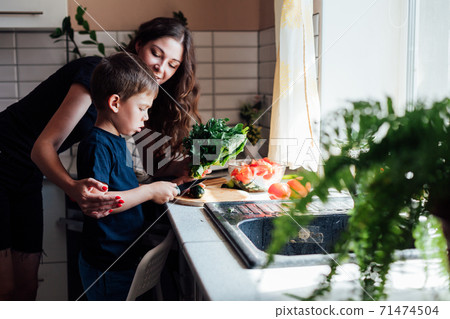 Beautiful mom and son cut fresh vegetables for salad with a knife 71474504