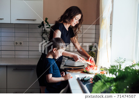 Beautiful mom and son cut fresh vegetables for salad with a knife 71474507