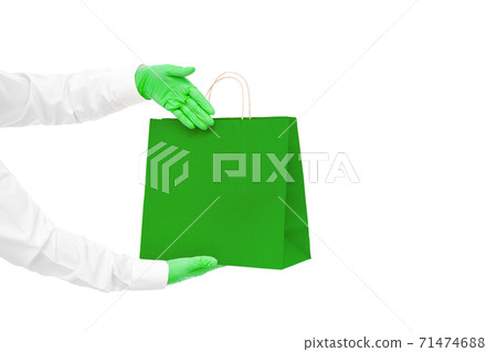 hands in green sterile gloves of faceless courier for safe delivery of eco food in green package shows palm at packet during quarantine of social distance isolated on white with copy space. hands in green sterile gloves of faceless courier for safe delivery of eco food in green package shows palm at packet during quarantine of social distance isolated on white with copy space. 71474688