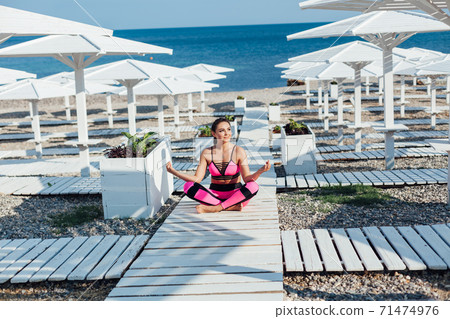 Beautiful fashionable brunette woman does fitness yoga on the beach by the sea 71474976
