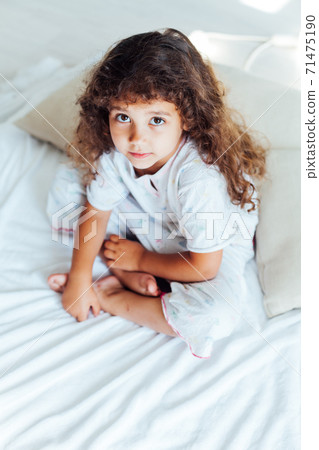 Beautiful little curly girl in the bedroom on the bed 71475190