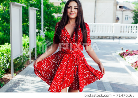 Beautiful fashionable brunette woman in a red summer dress walks in the street Beautiful fashionable brunette woman in a red summer dress walks in the street 71476163
