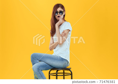 Pretty woman sits on a chair wearing sunglasses yellow background lifestyle Pretty woman sits on a chair wearing sunglasses yellow background lifestyle 71476381