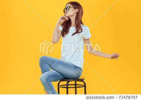 Pretty woman sits on a chair wearing sunglasses yellow background lifestyle Pretty woman sits on a chair wearing sunglasses yellow background lifestyle 71476707