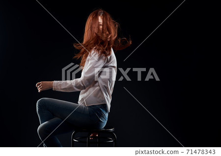 pretty woman sitting on a chair posing white shirt jeans long hair red lips dark background pretty woman sitting on a chair posing white shirt jeans long hair red lips dark background 71478343