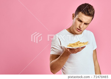 Man with French fries in a paper box on a pink background calories fast food portrait pink background Man with French fries in a paper box on a pink background calories fast food portrait pink background 71478465