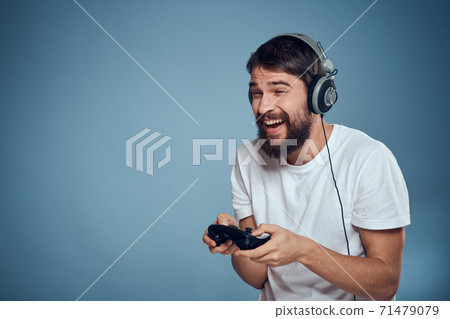 Man in headphones controller in hands playing game console lifestyle emotions blue background white t-shirt 71479079