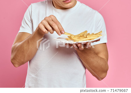 Man with French fries in a paper box on a pink background calories fast food portrait pink background Man with French fries in a paper box on a pink background calories fast food portrait pink background 71479087