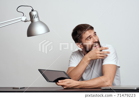 A man with a tablet at the table gestures with his hands on a light background and an iron lamp 71479223