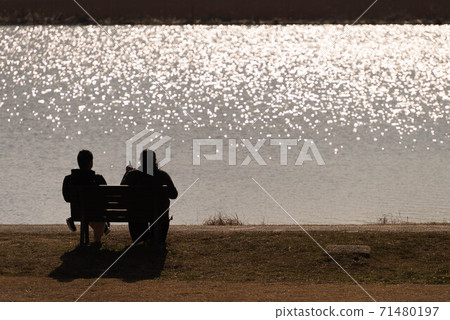 Father and son talking on a waterside bench 71480197