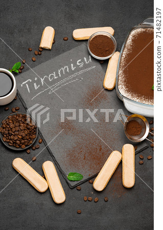 Traditional Italian Tiramisu dessert in glass baking dish, cup of coffee and savoiardi cookies on stone serving board with chalk inscription sign on concrete background 71482197