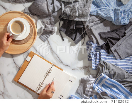 Woman is making daily to do list and schedule on notebook the organization of wardrobe in a closet. 71482982
