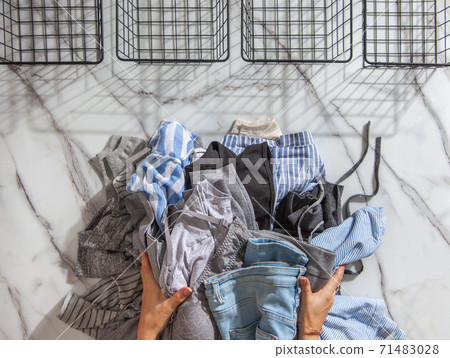 Woman hands putting stack of clean clothes for neatly tidying up and placing in steel wire wardrobe Woman hands putting stack of clean clothes for neatly tidying up and placing in steel wire wardrobe 71483028