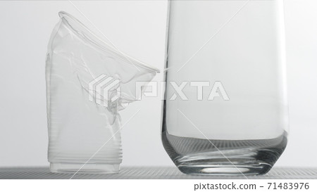 Collapsing plastic cup and a glass on light background. Sustainability of plastics concept 71483976