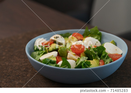 Salad with avocado, cherry tomatoes, romaine and mozzarella in blue bowl on walnut table with copy space Salad with avocado, cherry tomatoes, romaine and mozzarella in blue bowl on walnut table with copy space 71485283