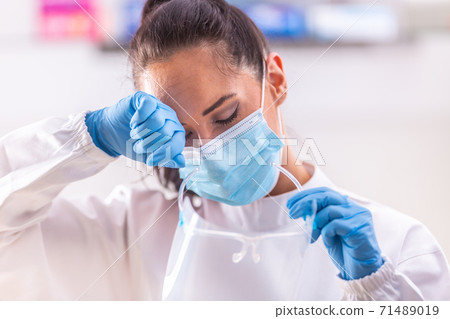 Exhaustion of medical staff worker wiping out sweat from forehead, holding protective goggles in hand, still wearing gloves and facemask Exhaustion of medical staff worker wiping out sweat from forehead, holding protective goggles in hand, still wearing gloves and facemask 71489019