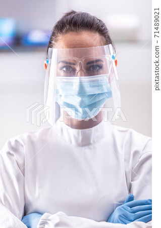Female doctor wearing protective gear such as shield, face mask and protective gloves 71489021
