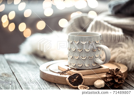 Coffee cup over Christmas lights bokeh in home on wooden table with sweater on a background and decorations. Holiday decoration Coffee cup over Christmas lights bokeh in home on wooden table with sweater on a background and decorations. Holiday decoration 71489807