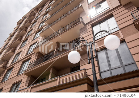 black iron lamp post with a white ball in the ceiling of a street lamp at the facade of a multi-storey building with a sun flare in the reflection of the window, close-up of architectural details. 71490104