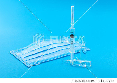 medical mask and syringe with ampoules for injection of a viral disease, conceptual background on the topic of pharmacology and vaccines for diseases with copy space on blue. medical mask and syringe with ampoules for injection of a viral disease, conceptual background on the topic of pharmacology and vaccines for diseases with copy space on blue. 71490548