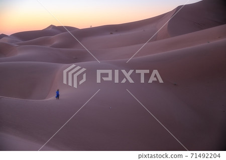 Unrecognizable Berber man walking on a dreamy desert at Twilight of dawn. Desert dune of Erg Chigaga, at the gates of the Sahara. Morocco. Concept of travel and adventure. 71492204