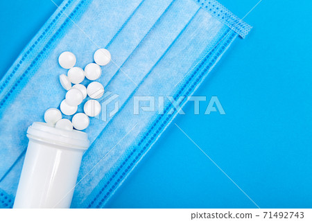 mock up sick mask with a bottle of a medical product with a scattered pile of pills on a blue background with copy space top view. mock up sick mask with a bottle of a medical product with a scattered pile of pills on a blue background with copy space top view. 71492743