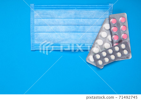 medical sick mask with a blister with pills on a blue background top view with copy space, conceptual background on a medical theme. medical sick mask with a blister with pills on a blue background top view with copy space, conceptual background on a medical theme. 71492745