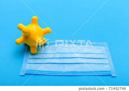 medical mask with yellow corona virus bacterium on a blue background with copy space, conceptual background on a medical theme mock up. medical mask with yellow corona virus bacterium on a blue background with copy space, conceptual background on a medical theme mock up. 71492746