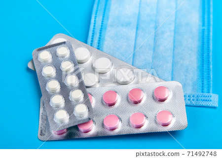 blisters with pills lying on a fabric medical mask on a blue background close up, medical background. blisters with pills lying on a fabric medical mask on a blue background close up, medical background. 71492748
