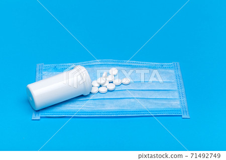 medical mask with a bottle of a medicinal product with a scattered pile of pills for the treatment of the respiratory tract of the lungs on a blue background with copy space. medical mask with a bottle of a medicinal product with a scattered pile of pills for the treatment of the respiratory tract of the lungs on a blue background with copy space. 71492749