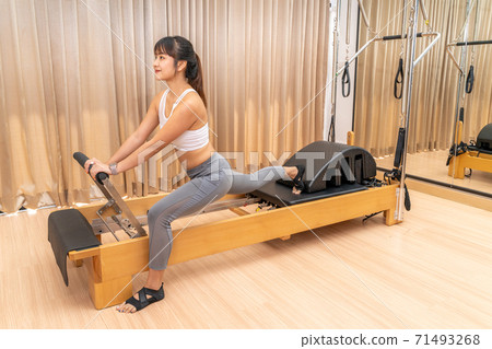 Young Asian woman working on pilates reformer machine during her health exercise Young Asian woman working on pilates reformer machine during her health exercise 71493268