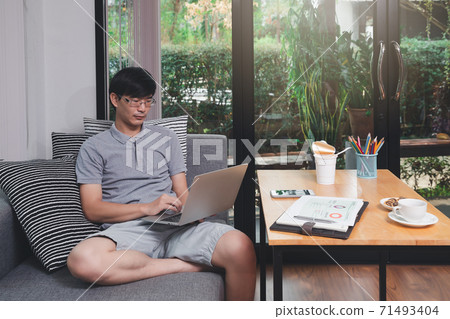 A man in casual wear using laptop while he is remotely working at home office. A man in casual wear using laptop while he is remotely working at home office. 71493404
