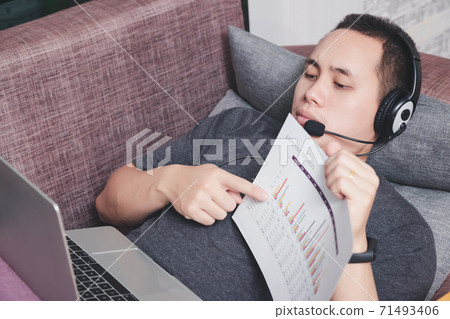 Young man lying on the couch and video call with colleagues by laptop in home office. Young man lying on the couch and video call with colleagues by laptop in home office. 71493406