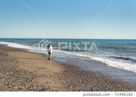 Young teen boy walking along shoreline of beach Young teen boy walking along shoreline of beach 71496182