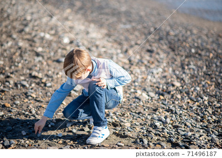 A boy collects seashells on the beach. Child playing on the beach. A boy collects seashells on the beach. Child playing on the beach. 71496187