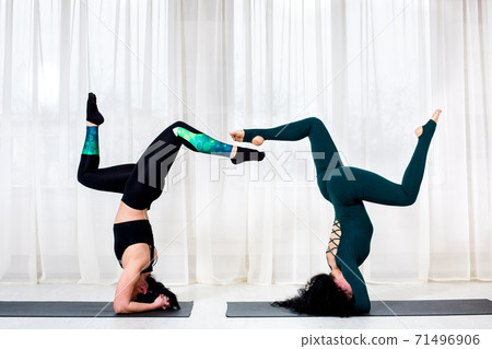 two girls go in for quarantine at home during the coronavirus pandemic and stands in a pose of a shirshasan asana upside down on a white floor in the room. 71496906