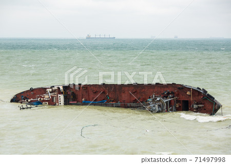 a cargo ship a tanker ran aground and rolled over into the sea with waves in cloudy weather, a man-made disaster, pollution of the marine ecosystem by emissions from the vessel. a cargo ship a tanker ran aground and rolled over into the sea with waves in cloudy weather, a man-made disaster, pollution of the marine ecosystem by emissions from the vessel. 71497998