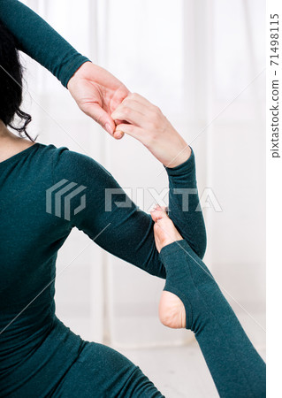 a woman on a dark green tracksuit stretches in a yoga pose in a room with a bright interior, close up detail arms and leg. 71498115