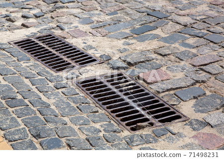 the 2 iron grates of the drainage system hatch on the road paved with paving stones, closeup of a sewer grates. the 2 iron grates of the drainage system hatch on the road paved with paving stones, closeup of a sewer grates. 71498231