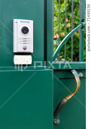 an intercom with a video camera and a microphone for voice communication with a card reader for access by a key card is installed on a green iron gate with handle. 71498236