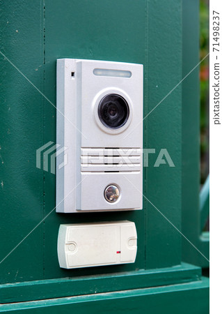 an intercom with a video camera and a microphone for voice communication with a card reader for access by a key card is installed on a green iron gate side view. 71498237