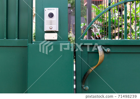 an intercom with a video camera and a microphone for voice communication with a card reader for access by a key card is installed on a green iron gate with handle, close up nobody. an intercom with a video camera and a microphone for voice communication with a card reader for access by a key card is installed on a green iron gate with handle, close up nobody. 71498239