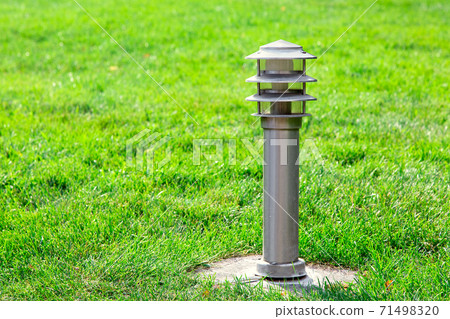 Ground iron streetlight electric lamp with bulb on green lawn with grass lit by sunlight. Ground iron streetlight electric lamp with bulb on green lawn with grass lit by sunlight. 71498320