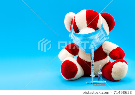 teddy bear in a medical mask with a syringe for vaccination and ampoules with a drug on a blue background with a copy space. teddy bear in a medical mask with a syringe for vaccination and ampoules with a drug on a blue background with a copy space. 71498638