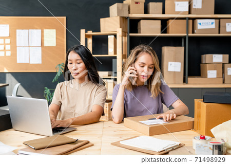 Young female manager of online shop office talking to clients on mobile phone Young female manager of online shop office talking to clients on mobile phone 71498929