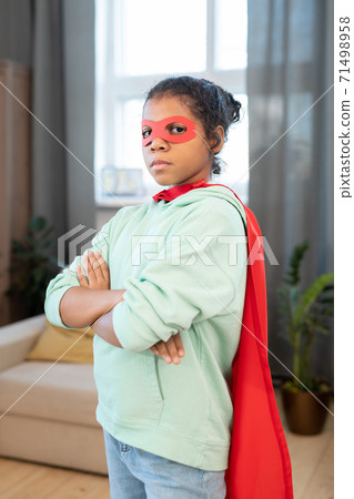 Adorable mixed-race girl in costume of superhero crossing arms on chest 71498958